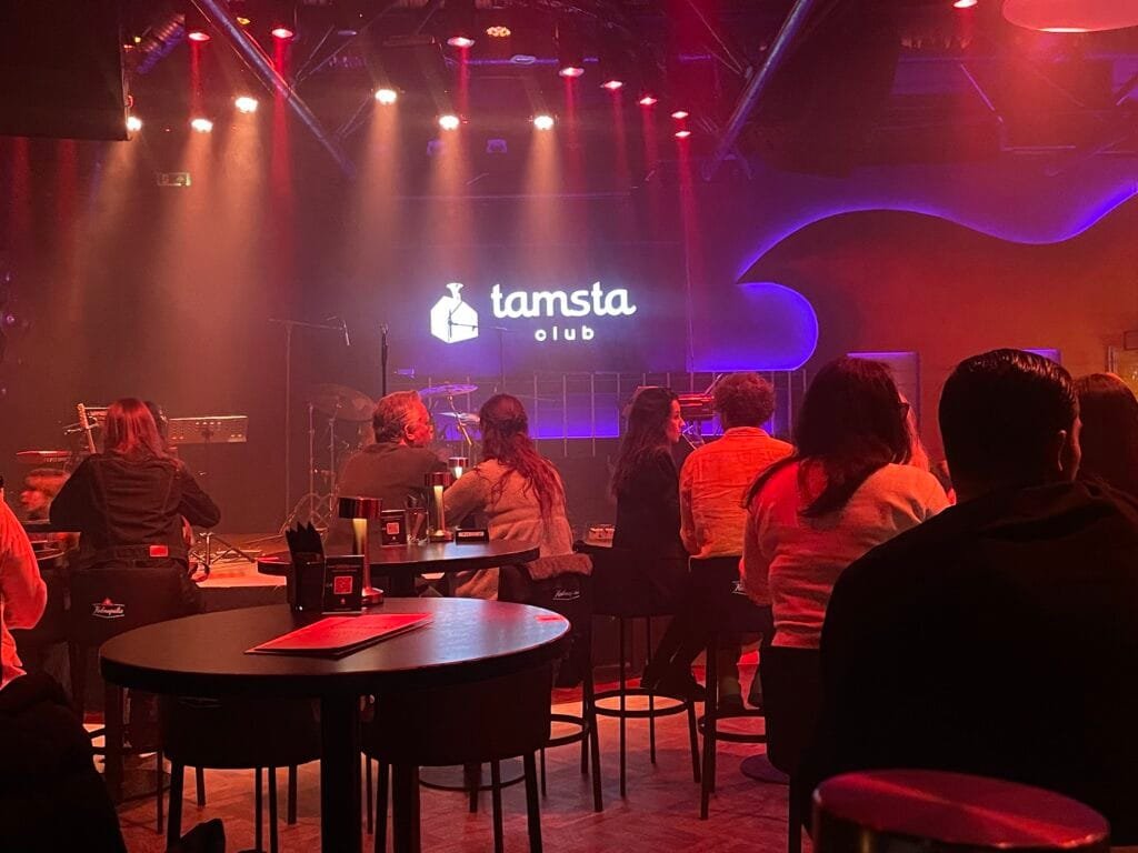 A live band performing on stage at Tamsta Club in Vilnius, with a lively crowd enjoying the concert atmosphere.