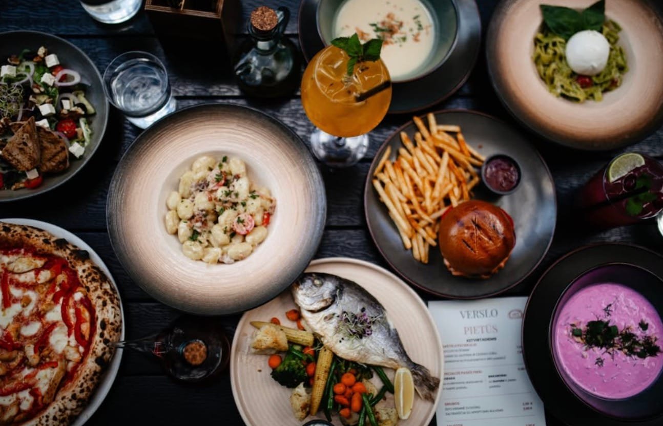 A rich table spread with pizza, pasta, burger, and fish dishes at 400 Laipsnių restaurant in Kaunas.