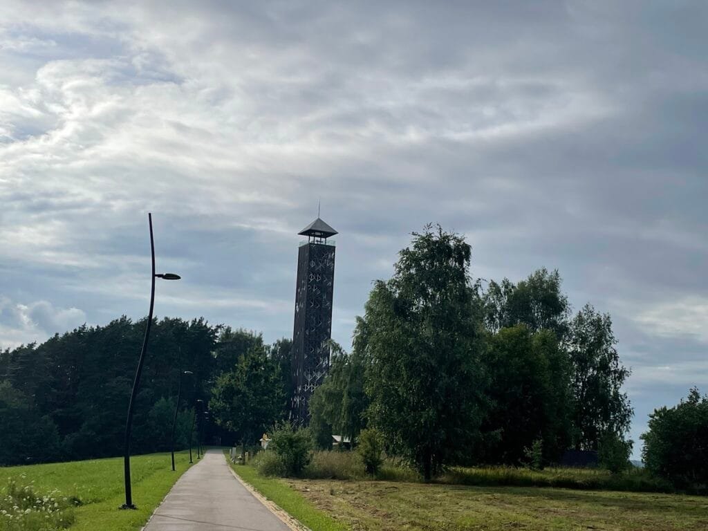 Tall Birštonas observation tower surrounded by trees along a path on a cloudy day.