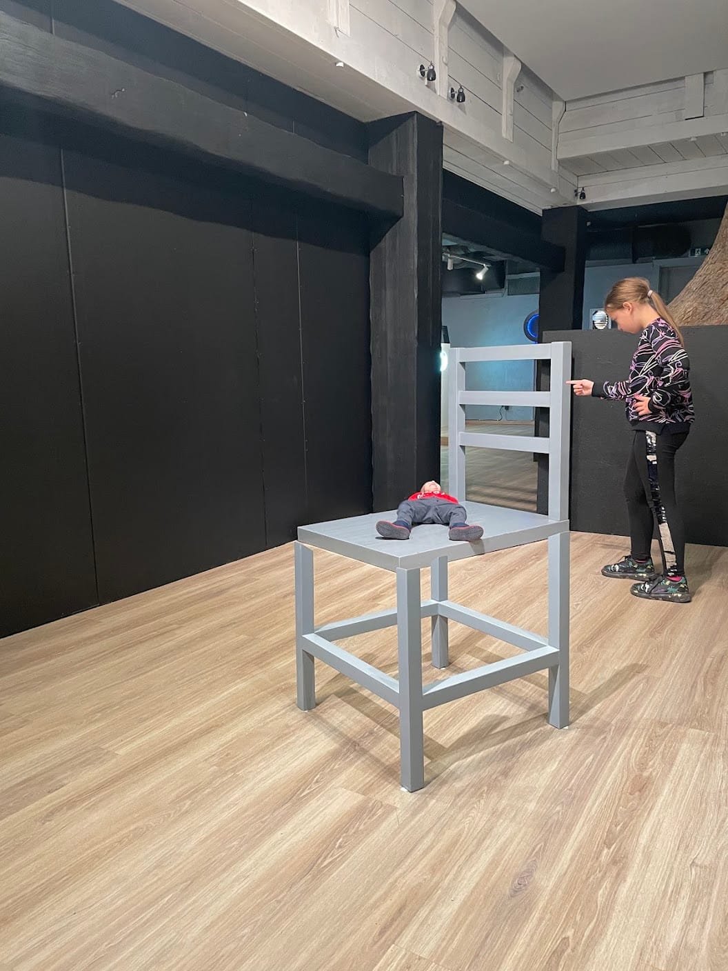 A child lying on a giant chair exhibit at the Museum of Illusions.
