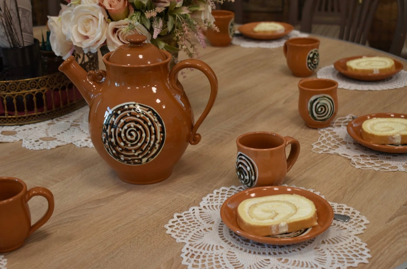 Clay pitcher, cups, and Swiss roll slices on a table at Kuršėnai Manor.