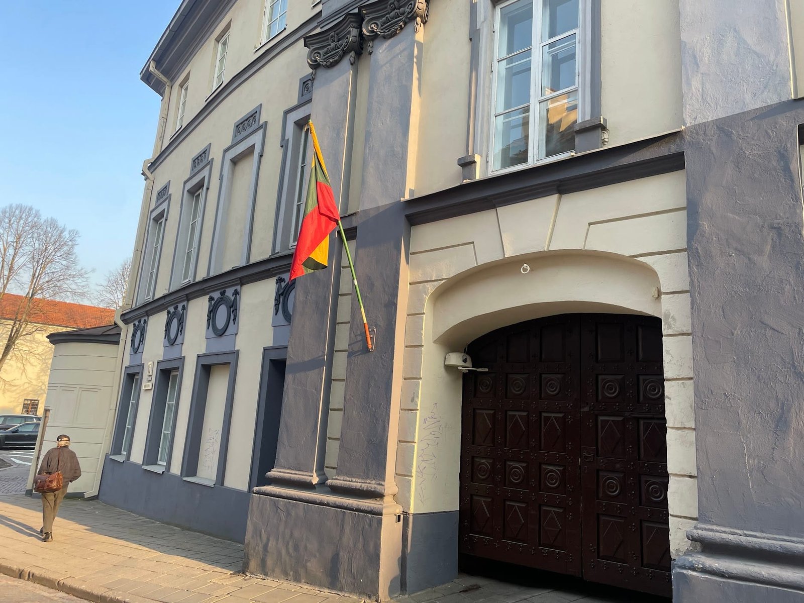 Lithuanian flag displayed on a historic building above a dark wooden gate.