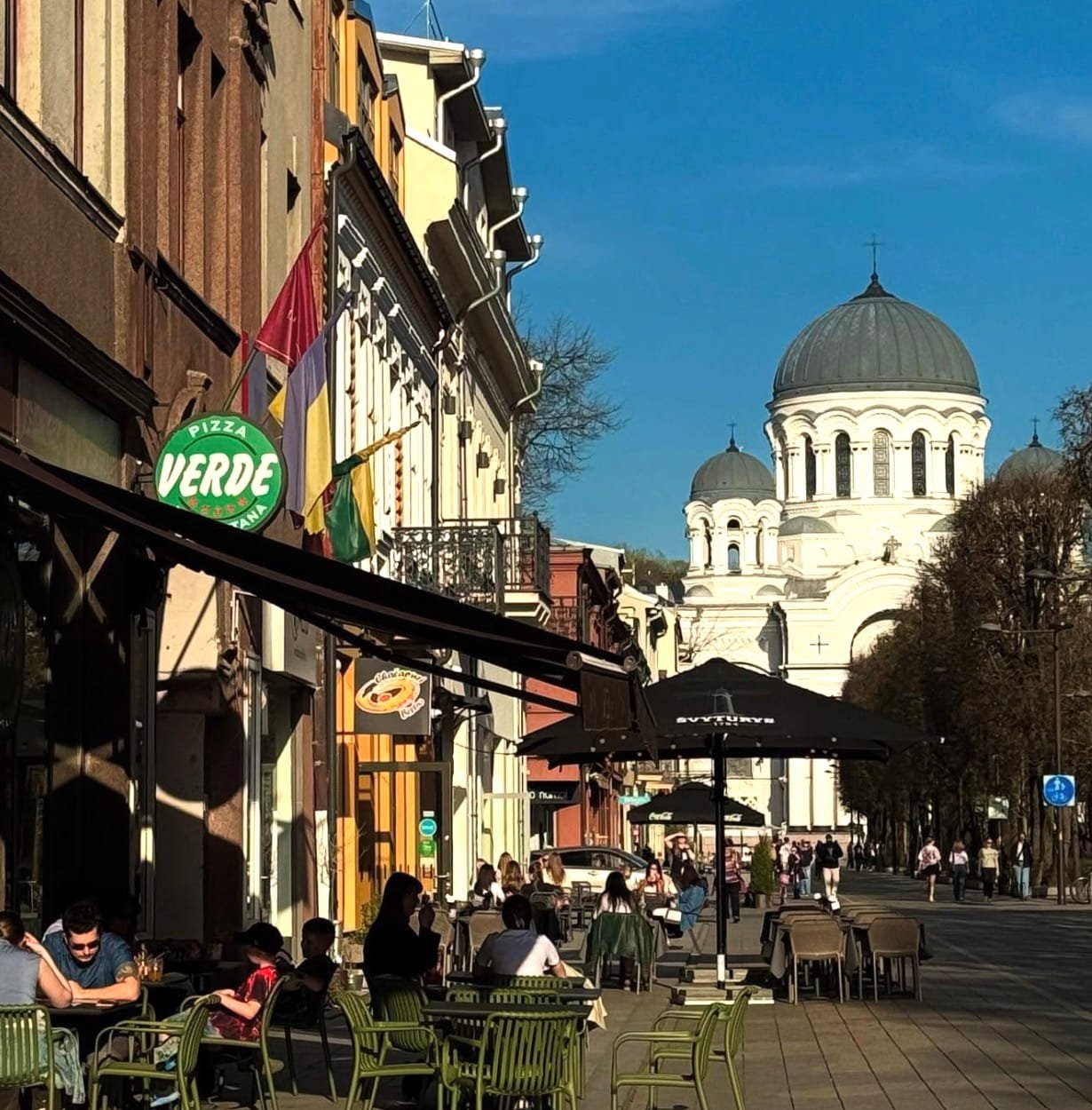 Outdoor seating along Laisvės Alėja near Pizza Verde with Church of St. Michael the Archangel in the background.