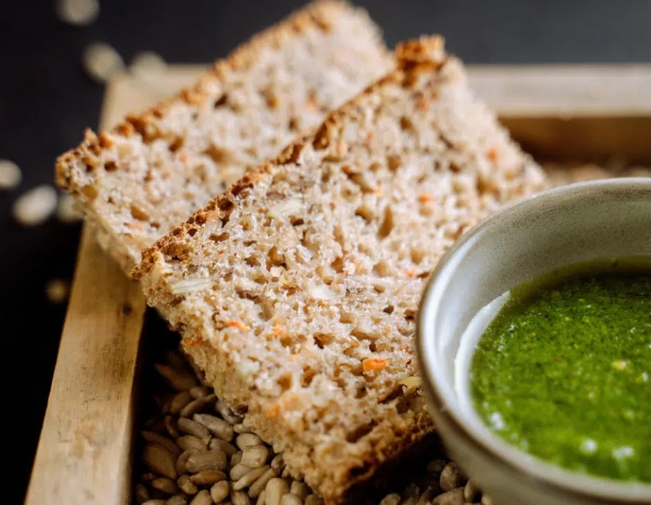 Whole grain seeded bread served with a side of green pesto sauce.