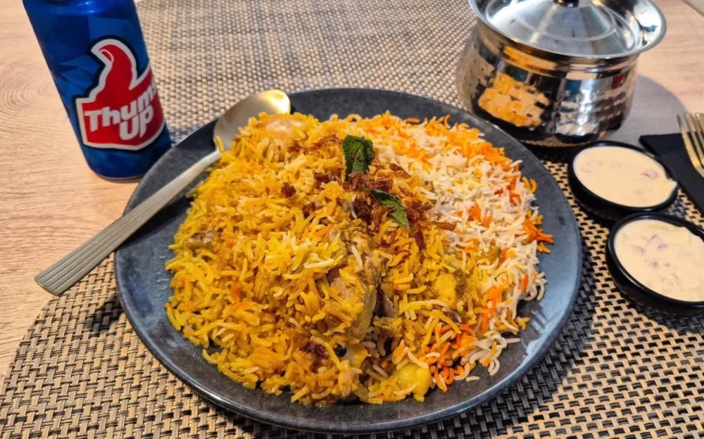 Plate of fragrant biryani rice served with raita and a can of Thums Up.