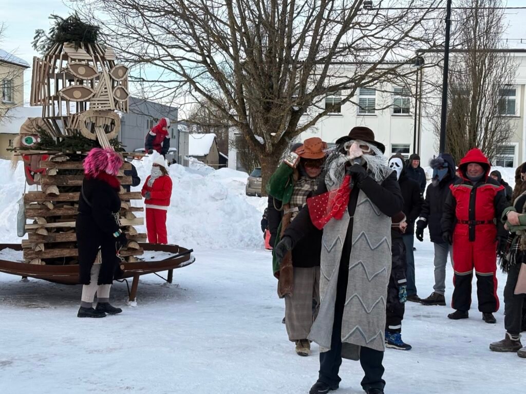 People in traditional masks celebrating Užgavėnės near a large effigy in winter.