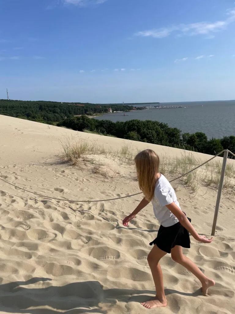 Girl walking barefoot on sandy sand dunes overlooking the Curonian Lagoon in Nida, Lithuania