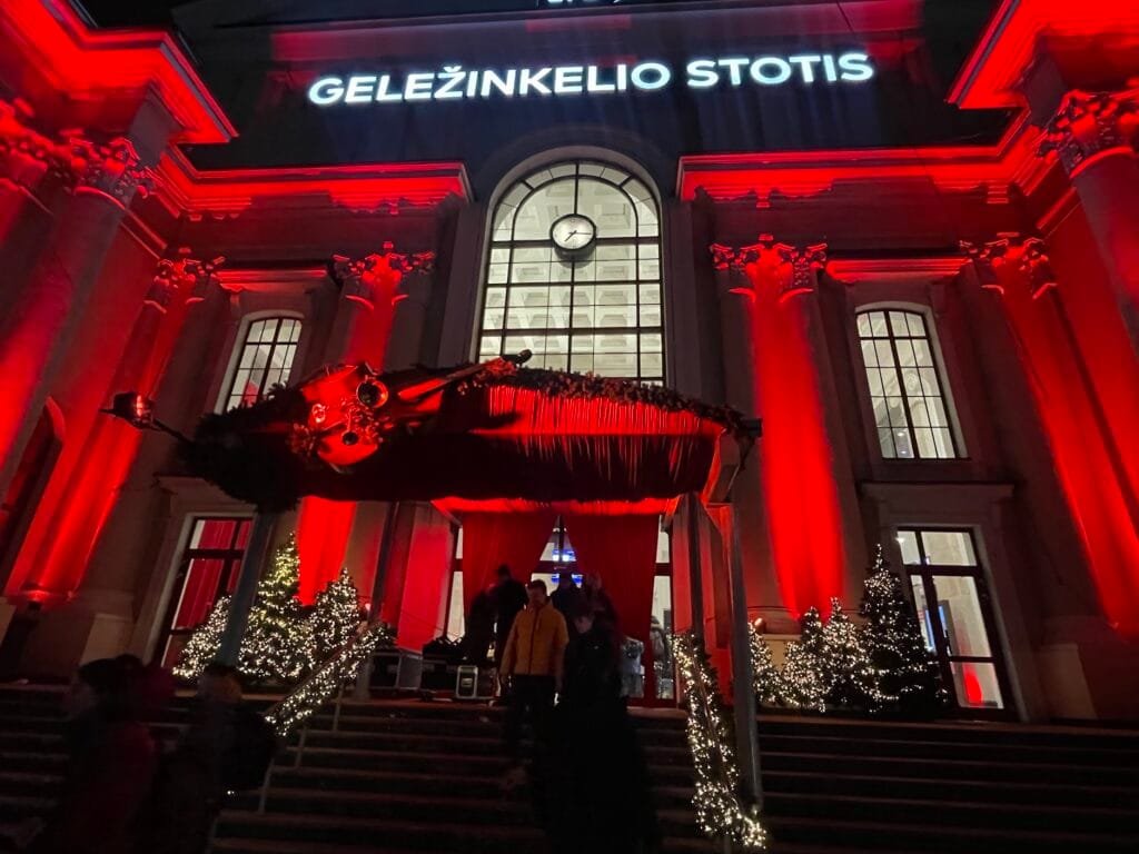 Raudonai apšviestas Vilniaus geležinkelio stoties pastatas su kalėdinėmis dekoraicijomis vakare.