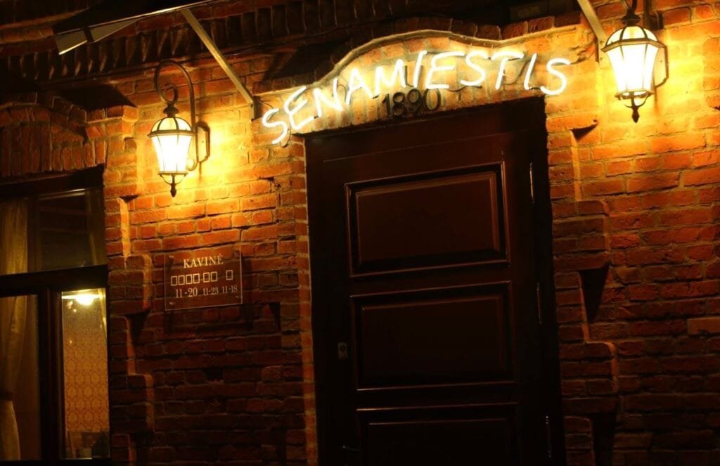 Cozy brick exterior and entrance of Senamiestis cafe illuminated at night in Telšiai.