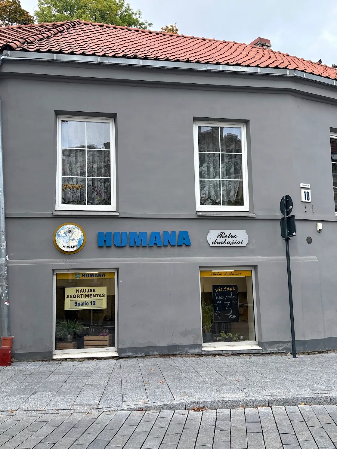 Exterior view of a Humana second-hand clothing store in a grey building.