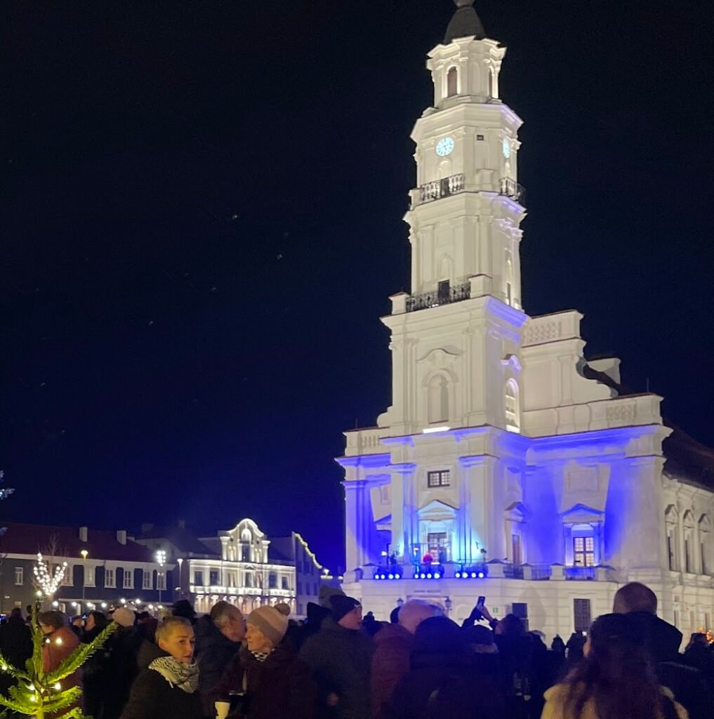 Illuminated Kaunas Town HallClick to open side panel for more information at night with crowds gathered in the square.