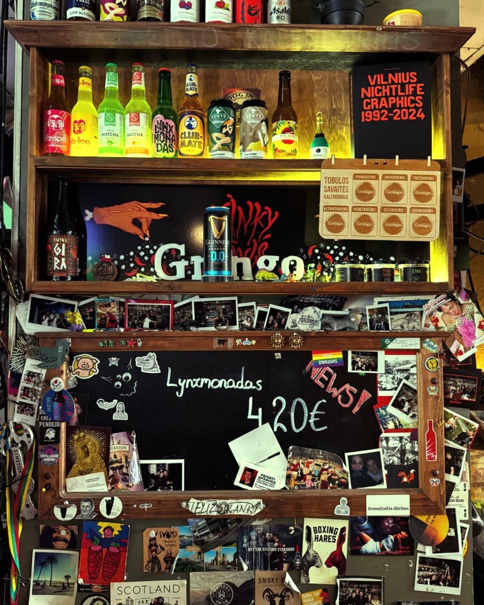 Bar shelf with drinks, photos, and a menu board at Gringo Pub in Vilnius.