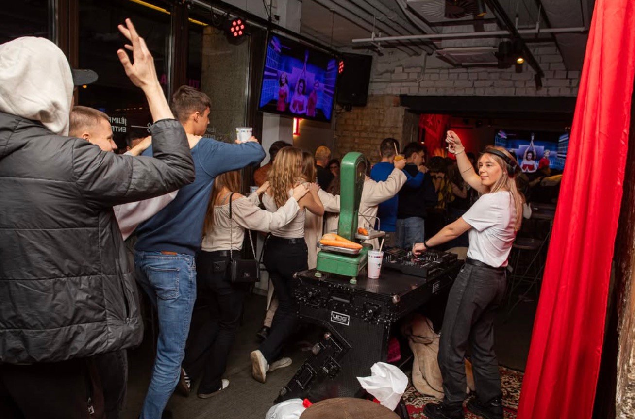 Crowd dancing at Plus Plus Plus pub in Vilnius with a female DJ playing music.