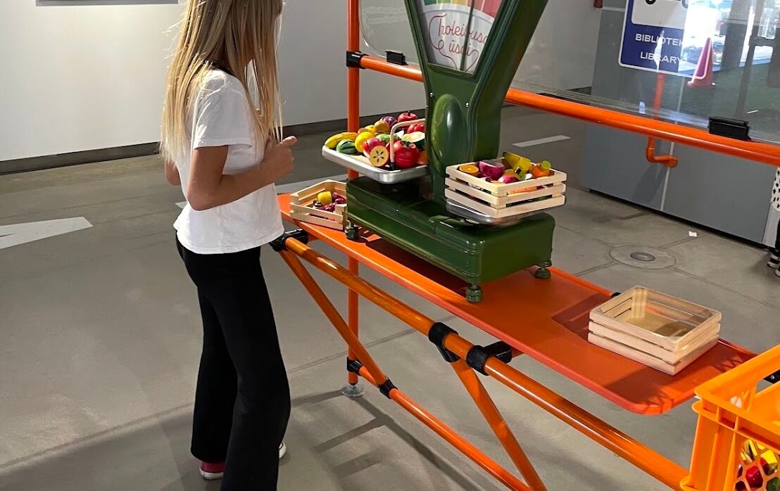 Girl playing with toy food scales at an interactive exhibit - museums in Kaunas for kids.