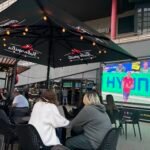 People sitting at outdoor tables watching sports on a large screen at sports bars in Vilnius