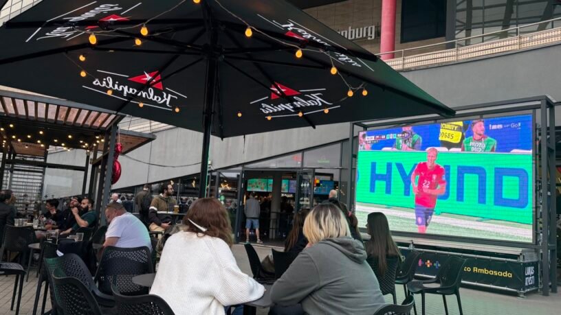 People sitting at outdoor tables watching sports on a large screen at sports bars in Vilnius